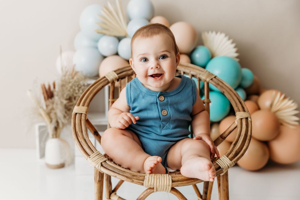 Baby sits in wooden rattan chair surrounded by pastel Easter eggs and spring decorations.