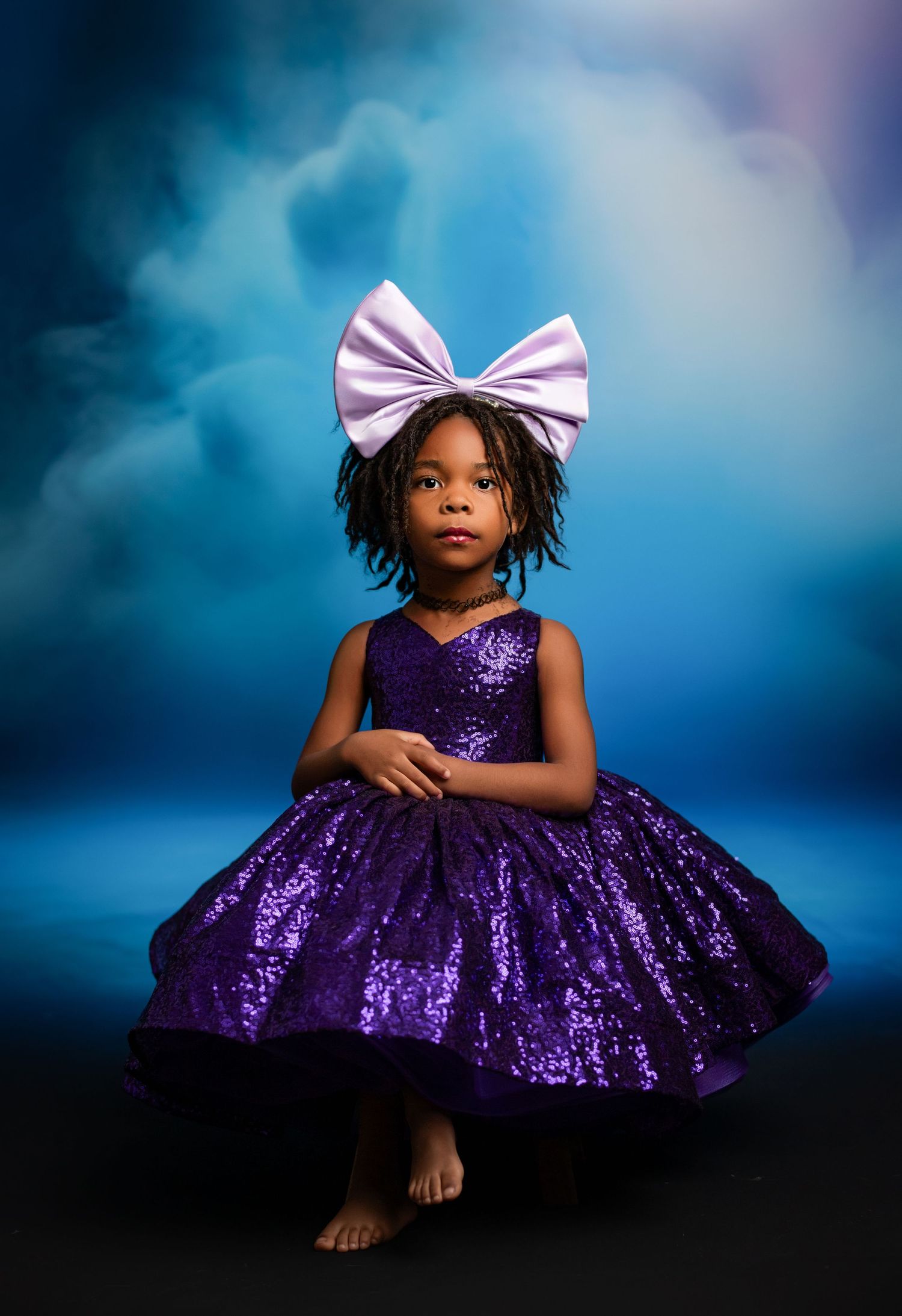 Whimsical lavender tulle dress captured against dreamy pink and purple clouds.