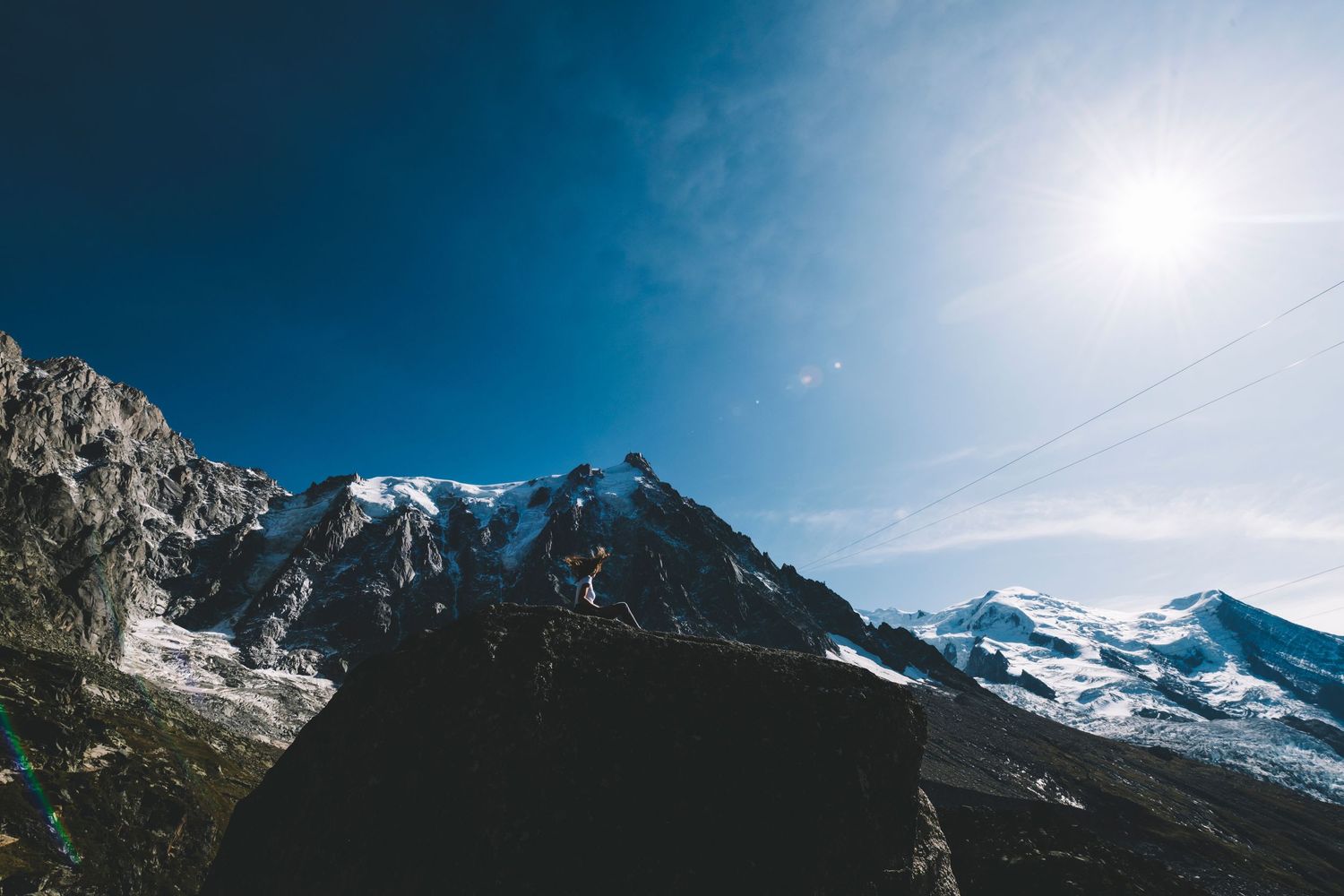 Snow-capped mountain peaks against deep blue sky with bright sun overhead.