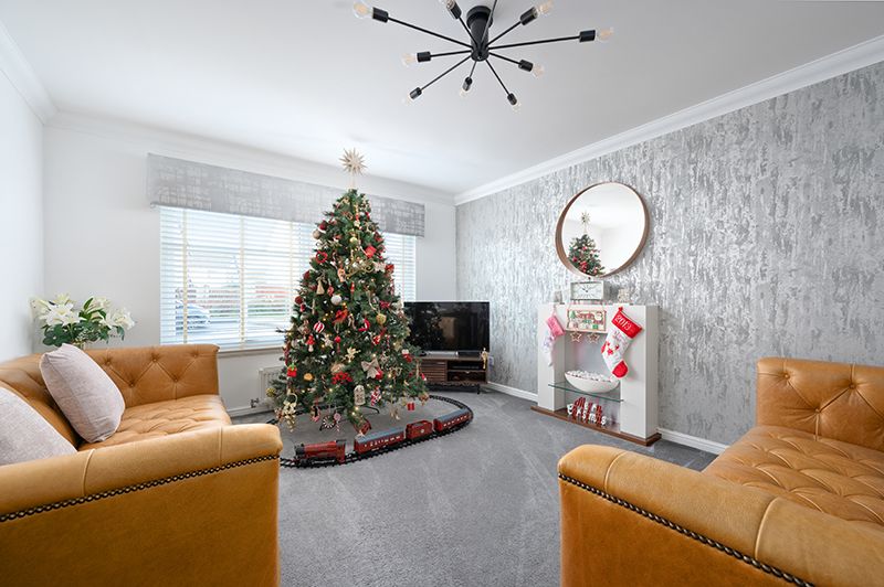 Modern living room with tan leather sofa, Christmas tree, and sputnik chandelier features elegant gray wallpaper.