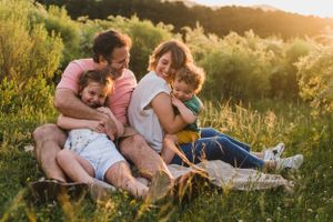 Familia sonriente sentada en una lona en la naturaleza en un sesión familiar durante el atardecer en Tandil