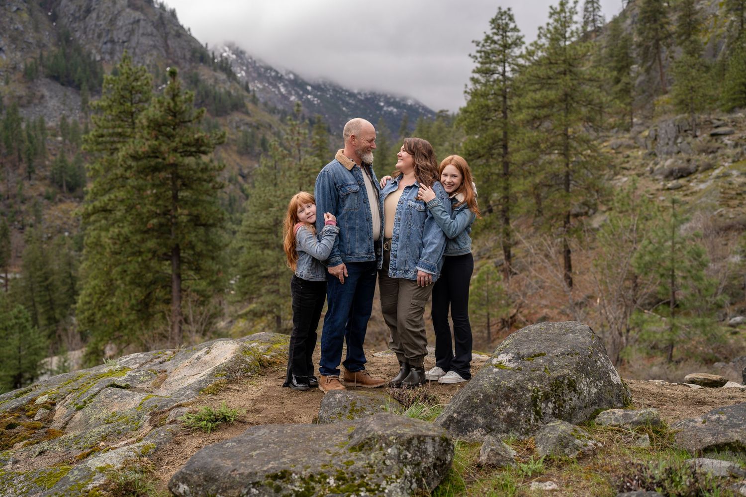 Group enjoying a scenic mountain view while standing on rocky terrain surrounded by evergreen trees.