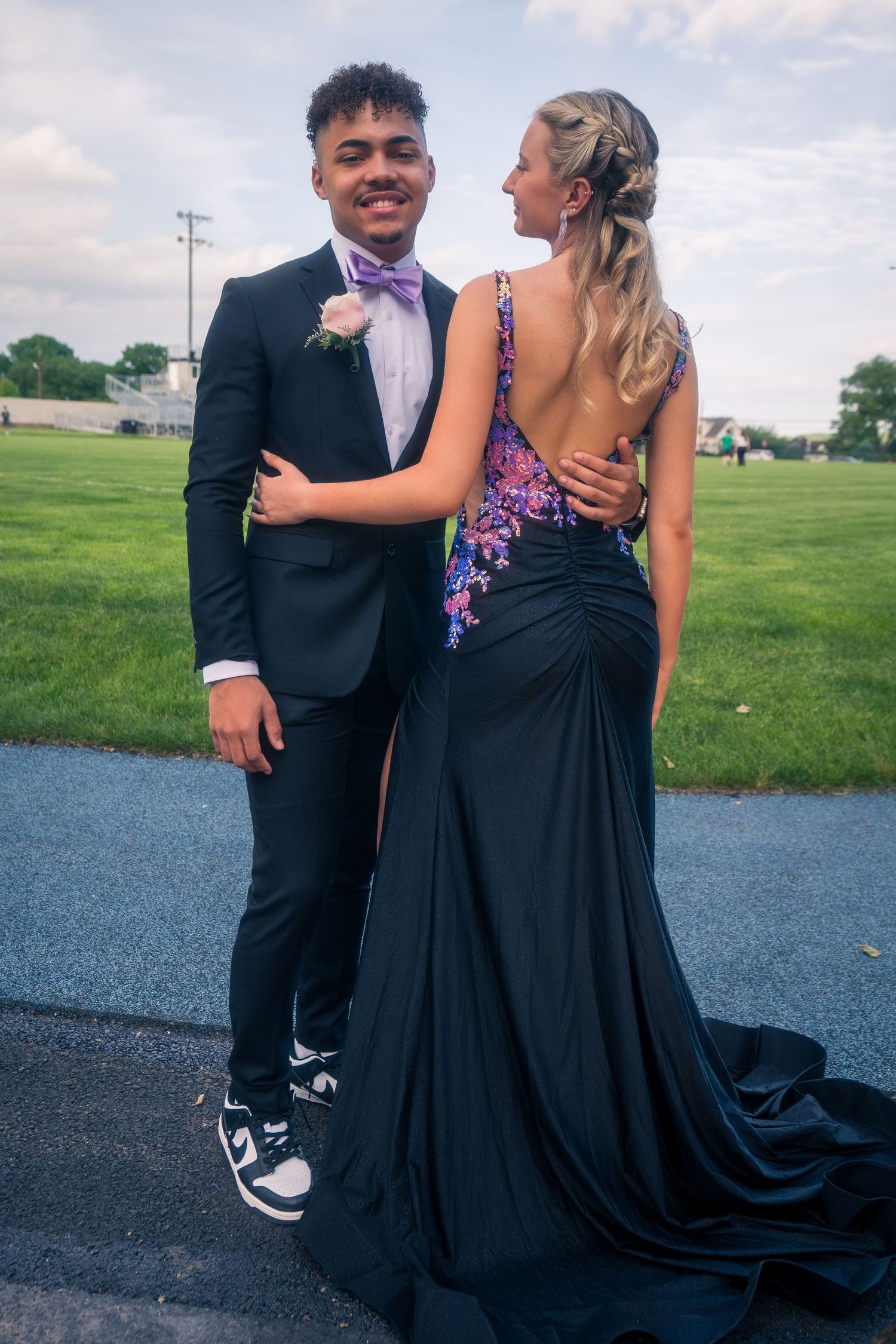 A couple in formal attire poses outdoors with the woman's dress featuring a dramatic train.