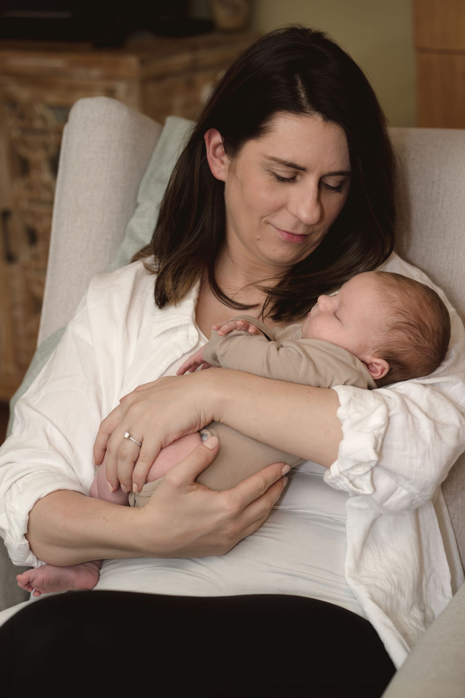 A tender moment between mother and newborn baby lying together on white bedding.