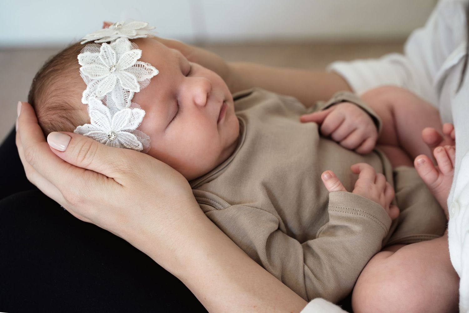 A sweet newborn baby wearing a floral headband resting on neutral bedding.