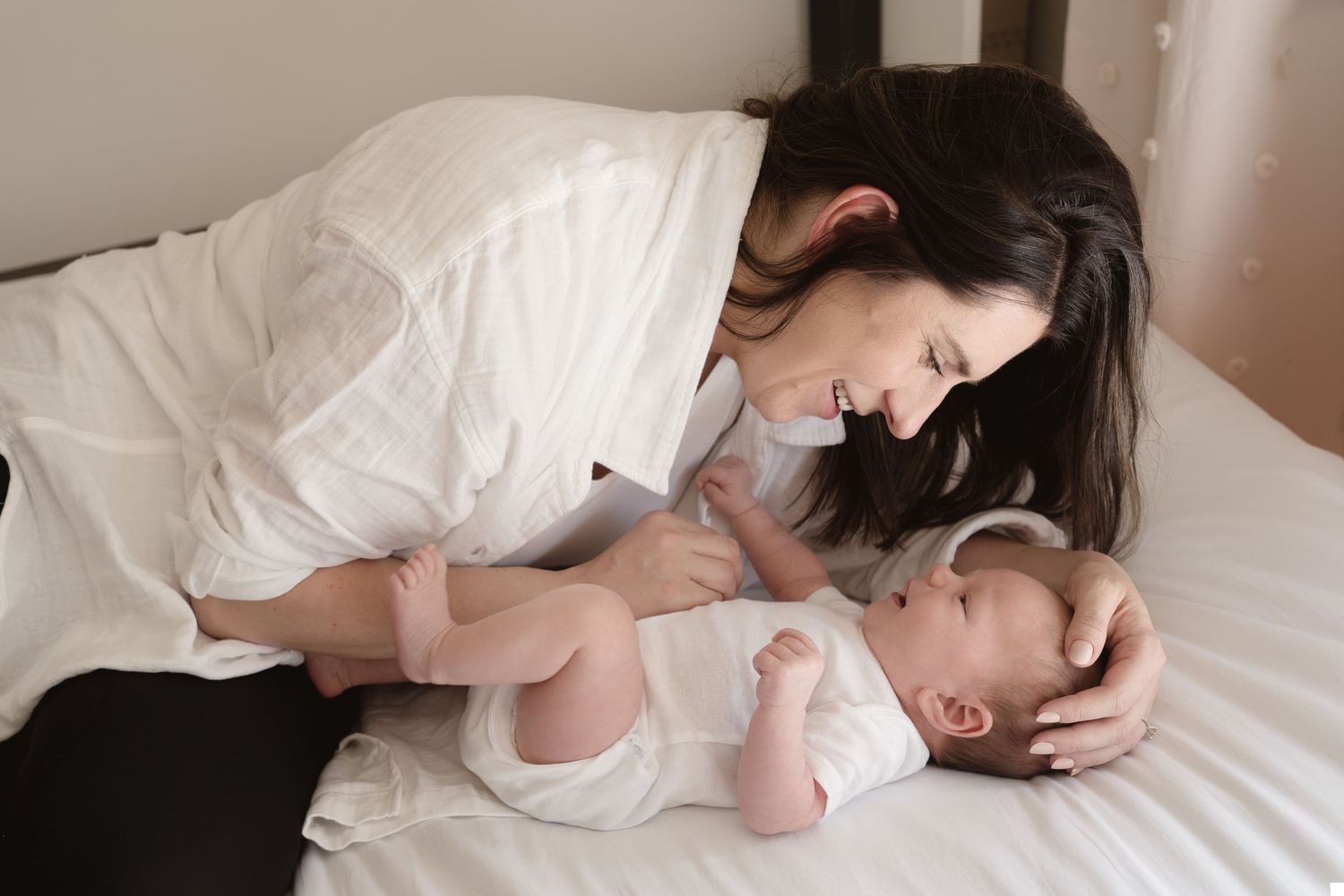 An intimate moment between parent and baby lying on white bedding indoors.