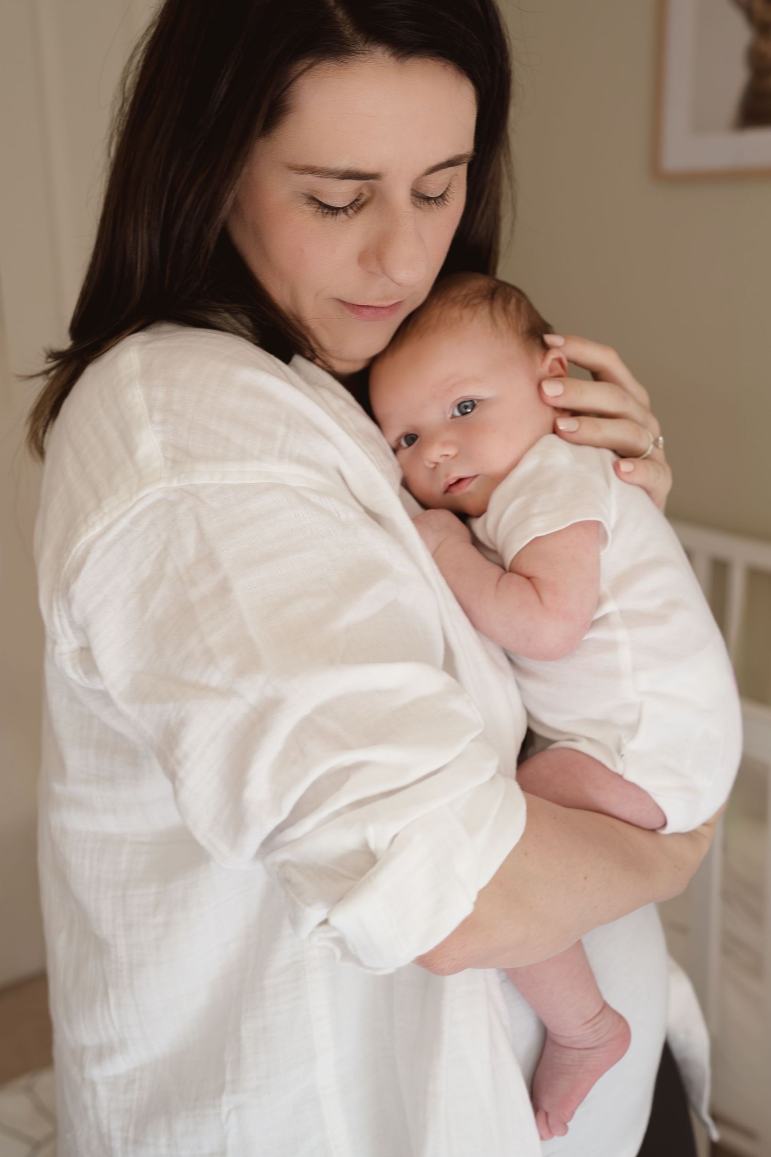 A peaceful indoor portrait of parent cradling a newborn baby while wearing white.