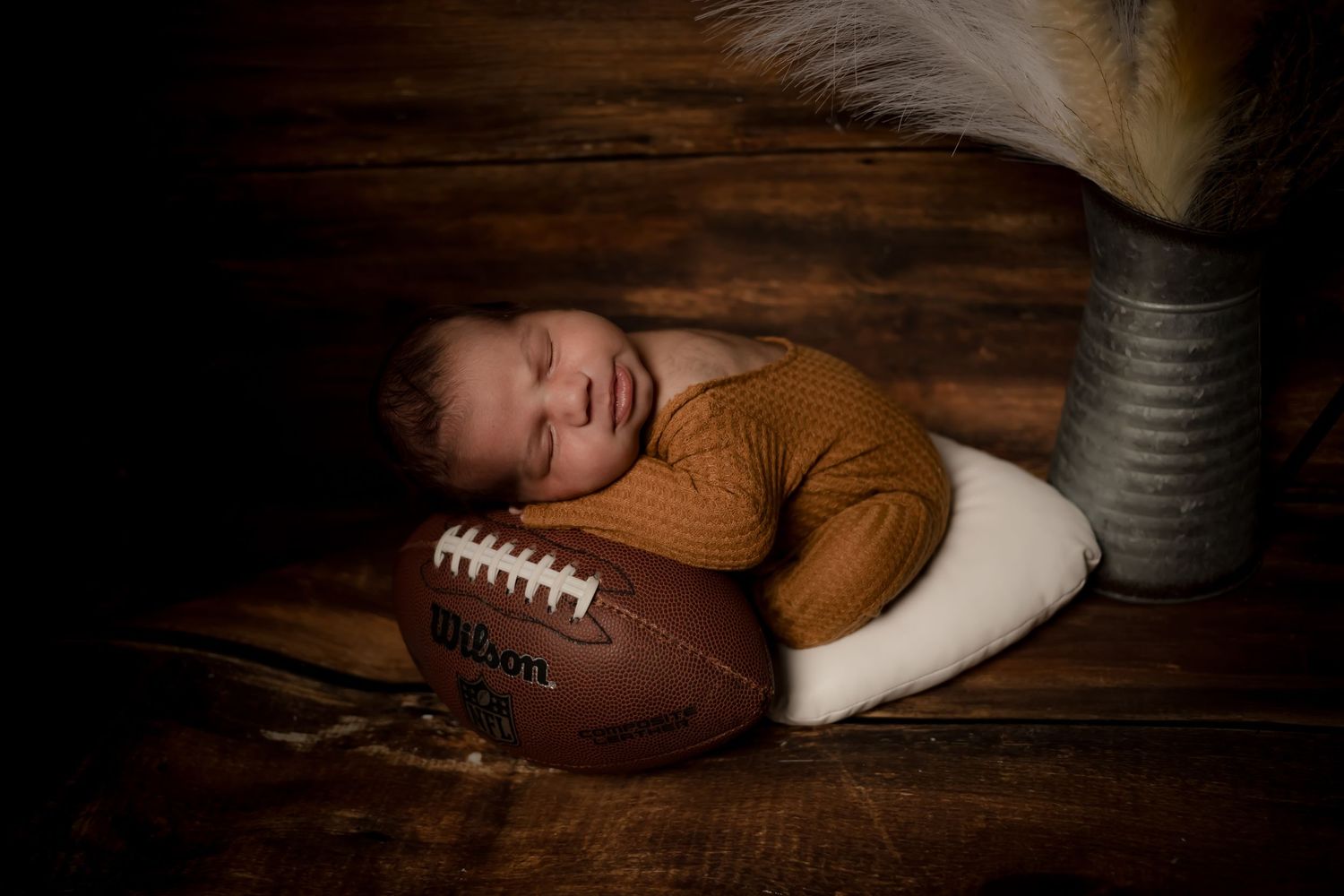 Baby resting head on football in moody artistic portrait.