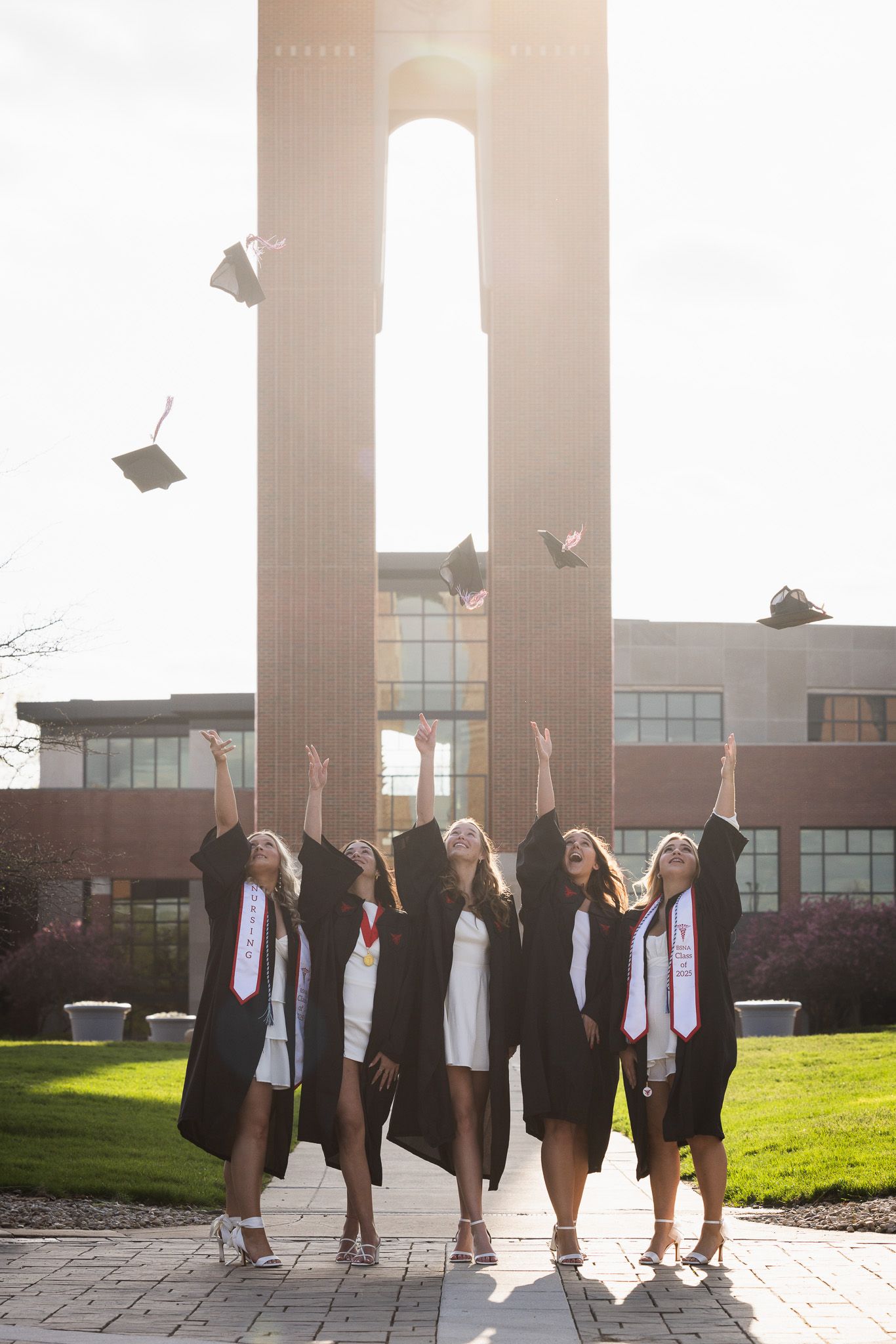 Graduates throw their caps in celebration against a modern building in golden sunlight.