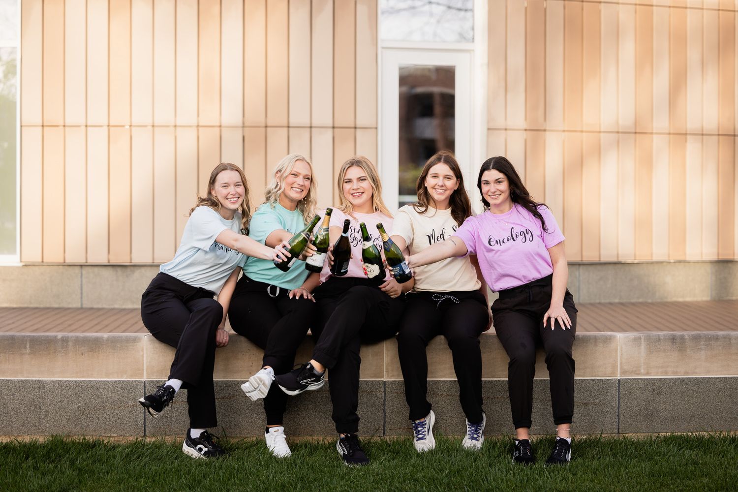 Group photo showing five friends sitting together on steps of a building in matching outfits.