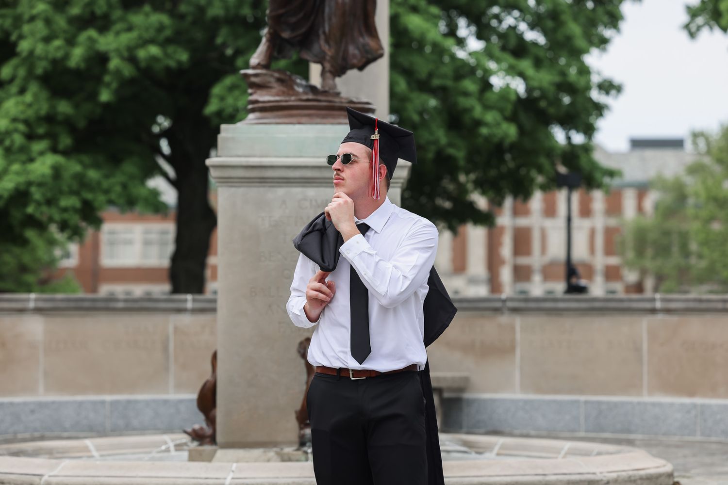 A graduate in formal attire celebrates with champagne near a classical stone column.