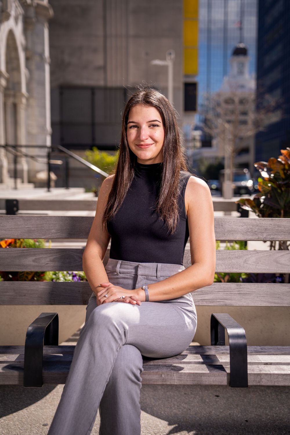 Young woman in black turtleneck and gray pants sitting on bench smiling in urban outdoor setting  in Tampa.