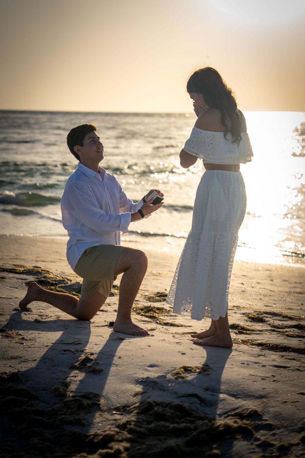 Man proposing to woman on bended knee at sunset beach with engagement ring in hand in Tampa.