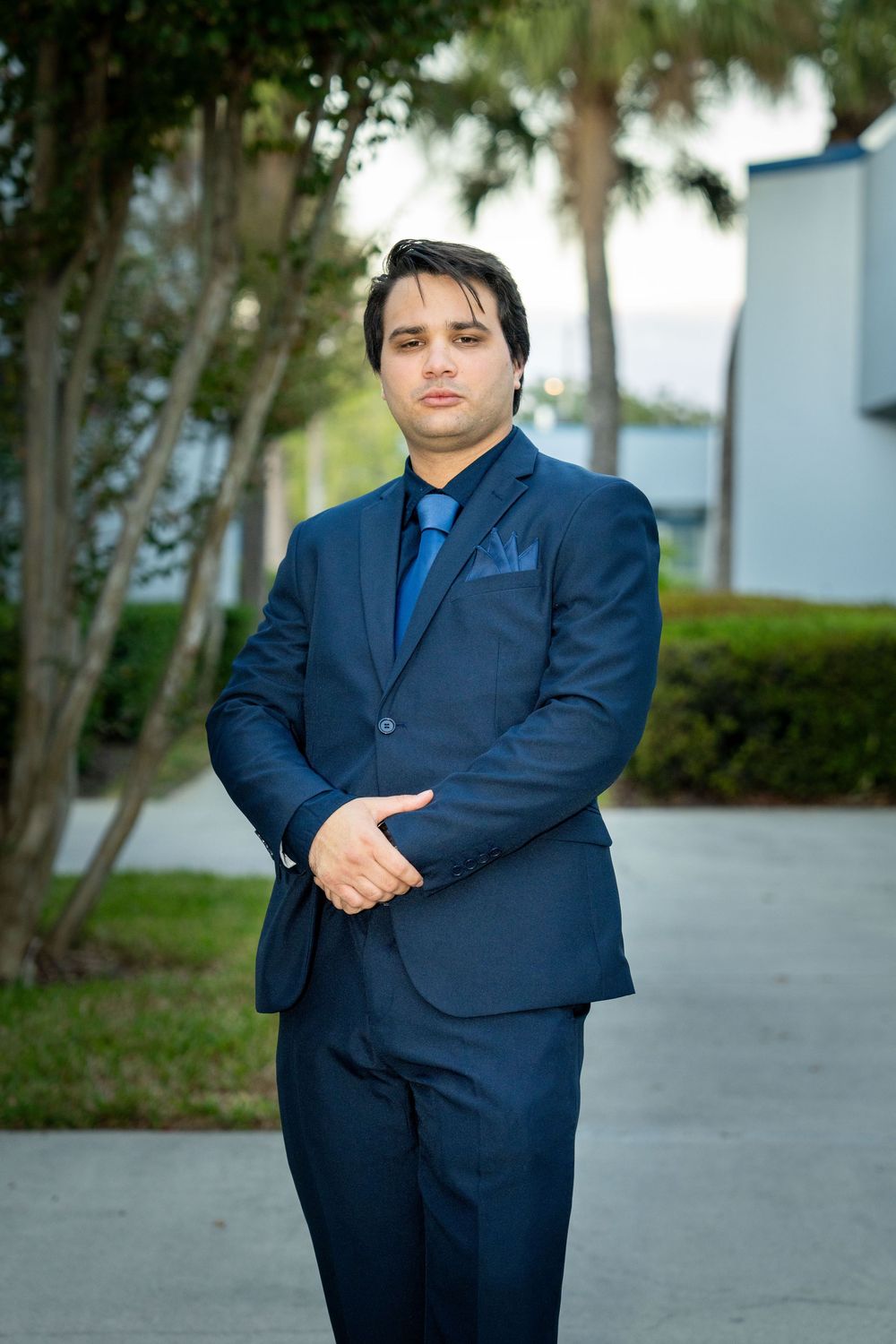 Professional man in navy blue suit and tie standing outdoors near palm trees for a business portrait in Tampa.