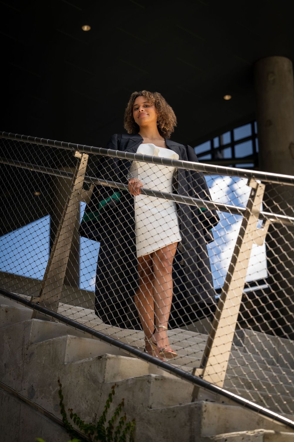 Professional woman in white dress and blazer posing on stairs by metal railing in urban setting in Tampa.