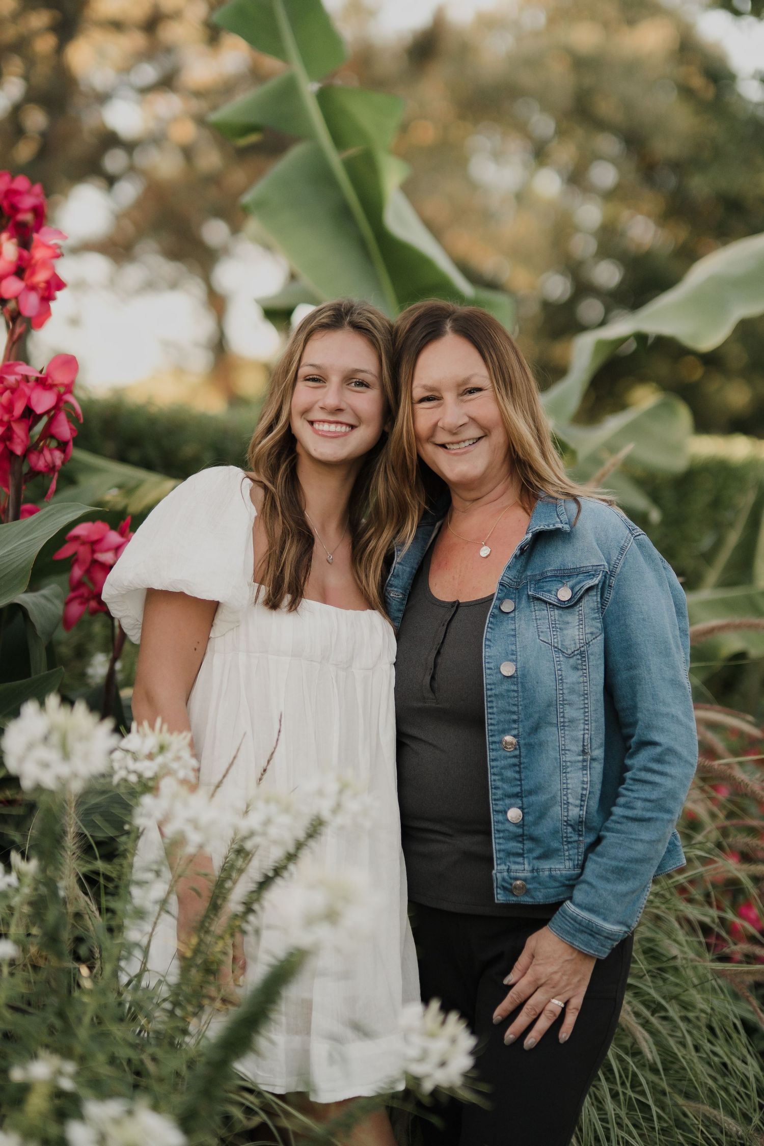 Two people smiling together in a garden with pink flowers and greenery.