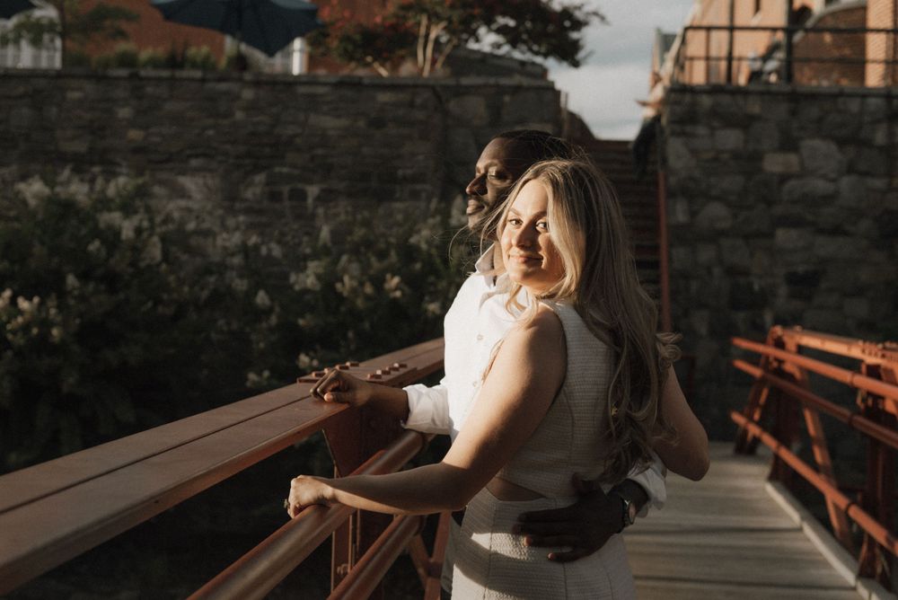 A person in white dress looking over their shoulder on a wooden bridge at sunset.