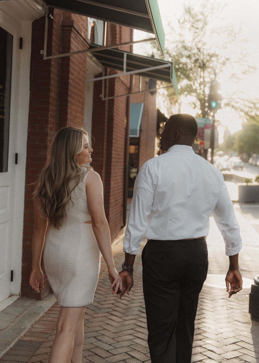 A couple strolling together through a charming brick-lined street during golden hour.