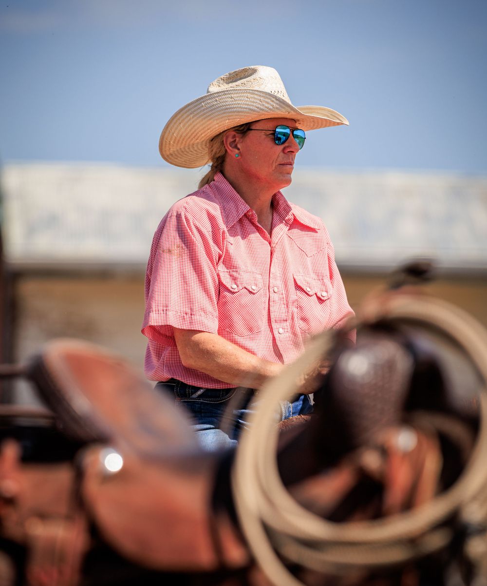 Rancher in pink shirt and cowboy hat observing from horseback.