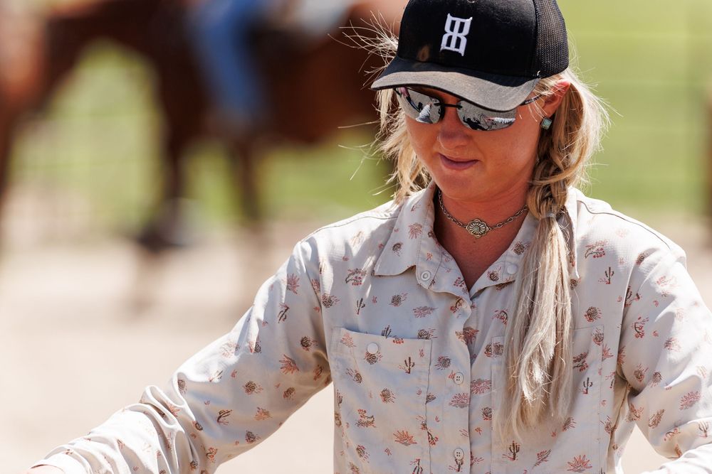 Rider in floral shirt and baseball cap during equestrian activity.