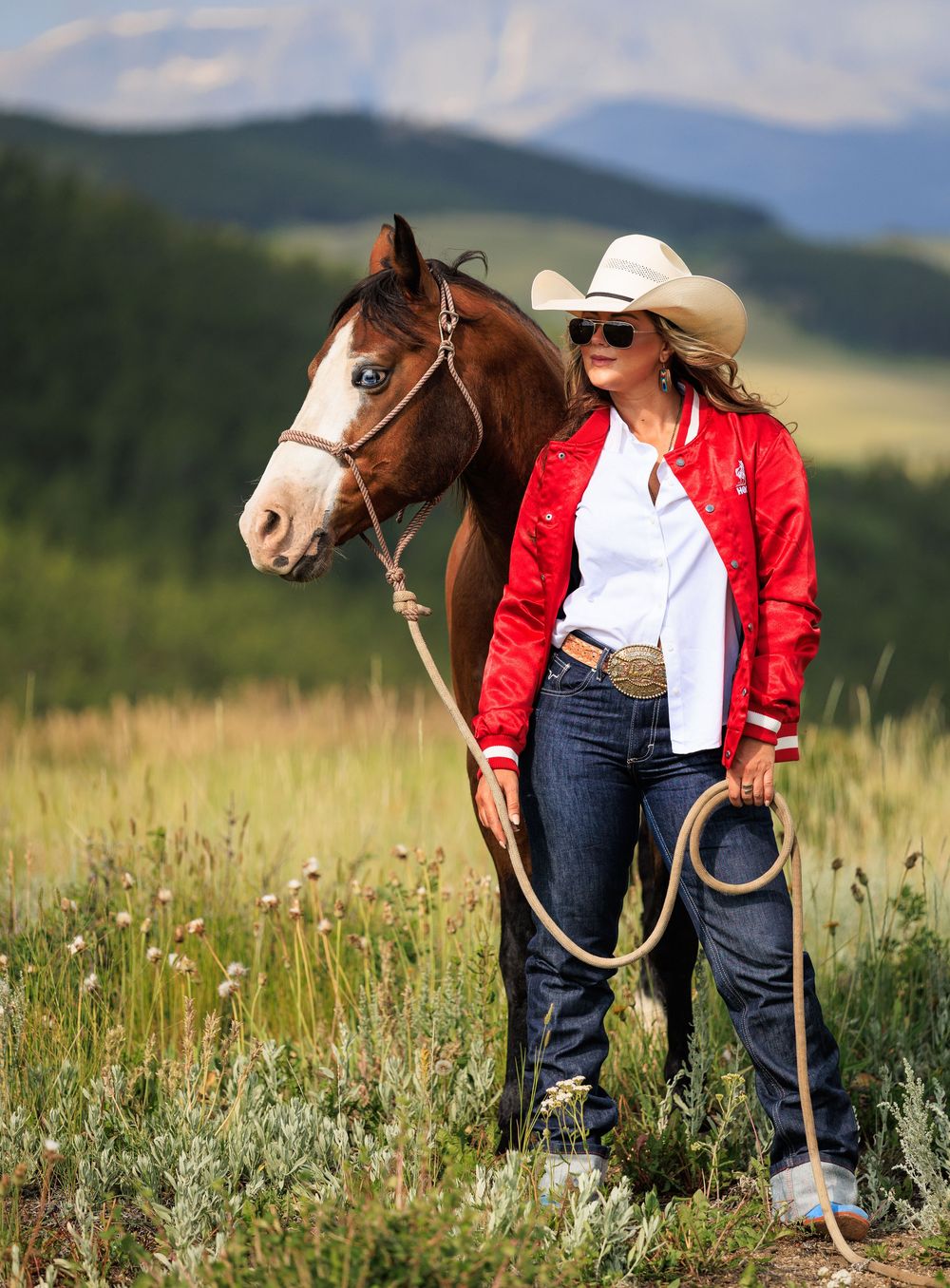 Horse and rider in red jacket against mountain landscape backdrop.
