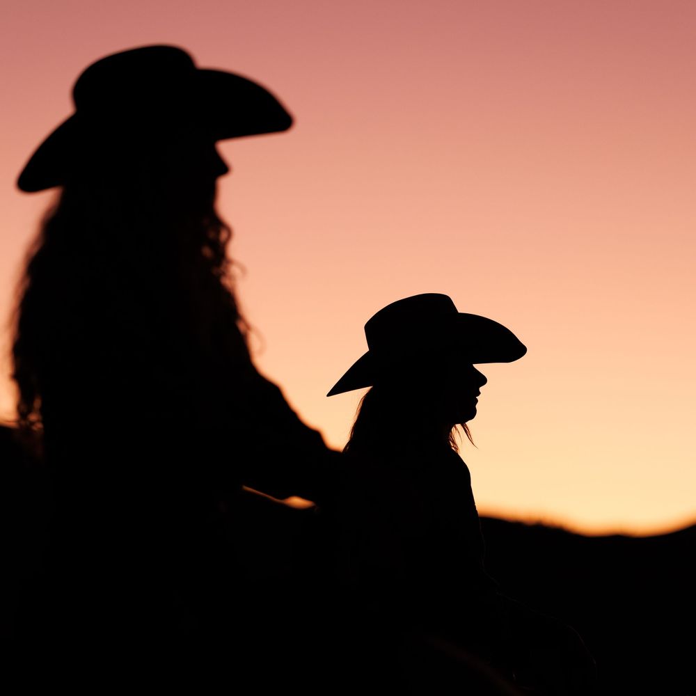 Silhouettes of cowboys on horseback against a vibrant sunset sky.