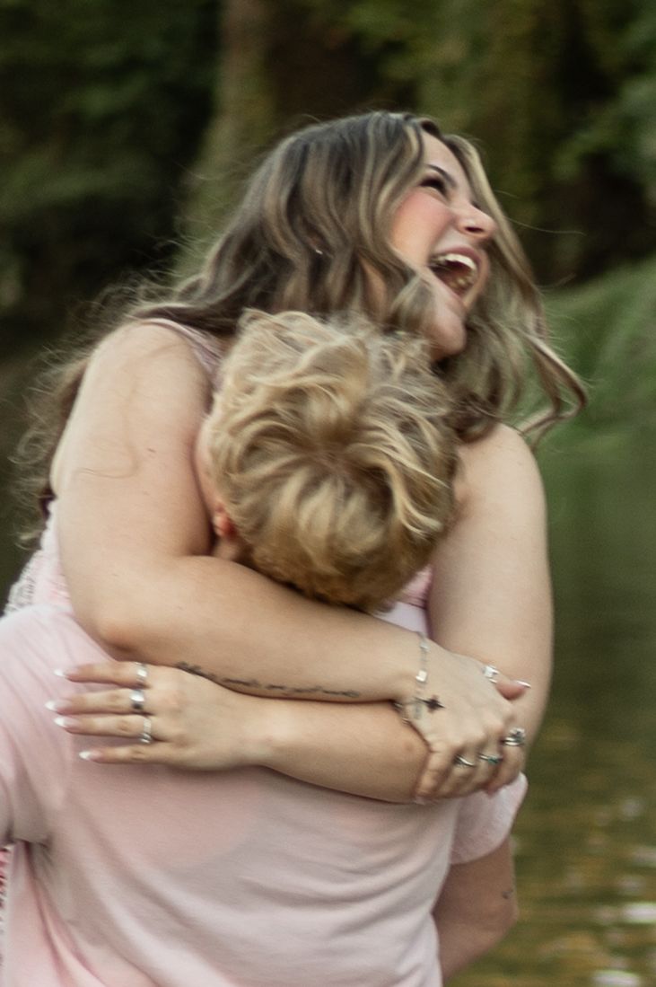 A couple in soft pink and beige clothing share an intimate embrace outdoors with a blurred natural background.