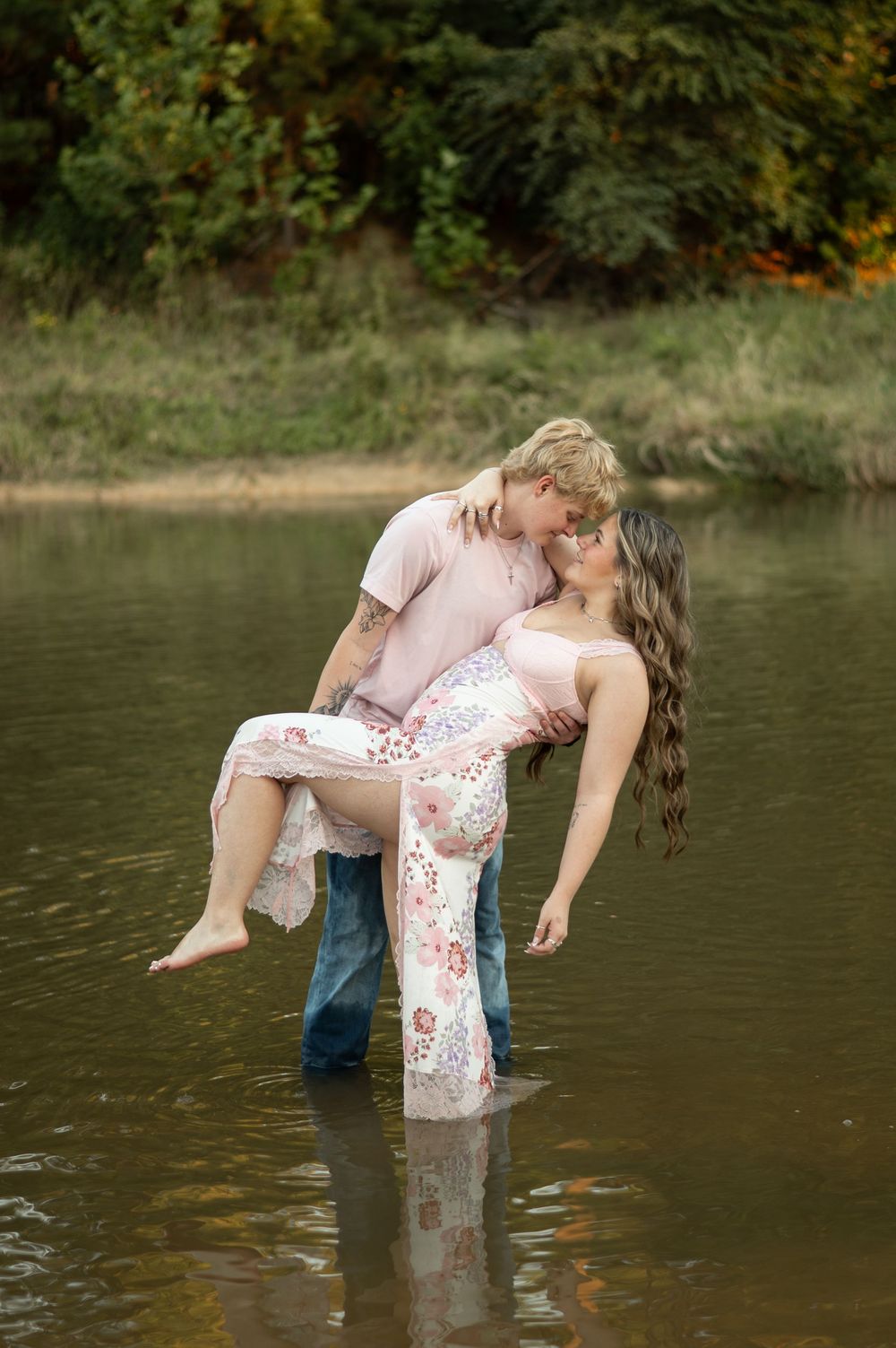 A romantic couple dips in a dramatic pose by a serene lake with autumn foliage in the background.