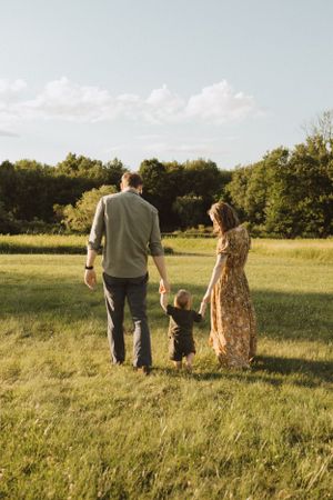 Family walking hand in hand through serene meadow at sunset.
