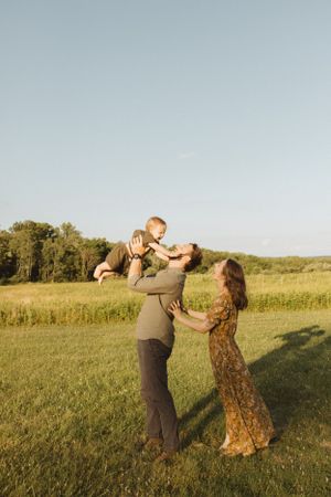 Parents playing with child in sunny meadow during golden hour photo session.