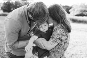 Parents sharing tender moment with their small child in black and white outdoor setting.
