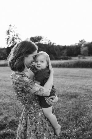 Mother in floral dress holds toddler close in black and white outdoor portrait.