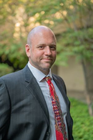 Professional headshots showing person in pinstriped suit with red tie against natural outdoor background.