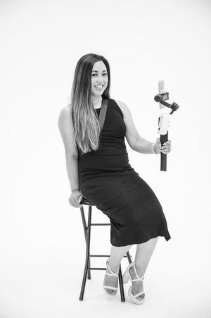 A person in a black dress sits on a stool in three different poses holding a wine bottle against a white background.
