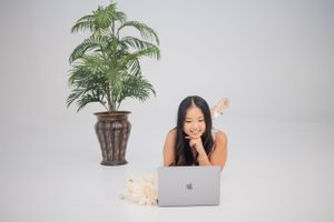 Minimalist workspace setting with palm plant and laptop against light gray background.