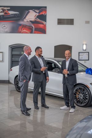 Two people in gray suits examining details of a luxury vehicle in a modern car showroom.