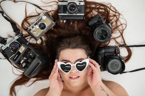 A collection of vintage film cameras arranged with flowing brown hair and sunglasses in a creative flat lay composition.