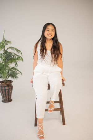 All-white professional outfit styled with strappy sandals in minimal studio setting with potted plant.