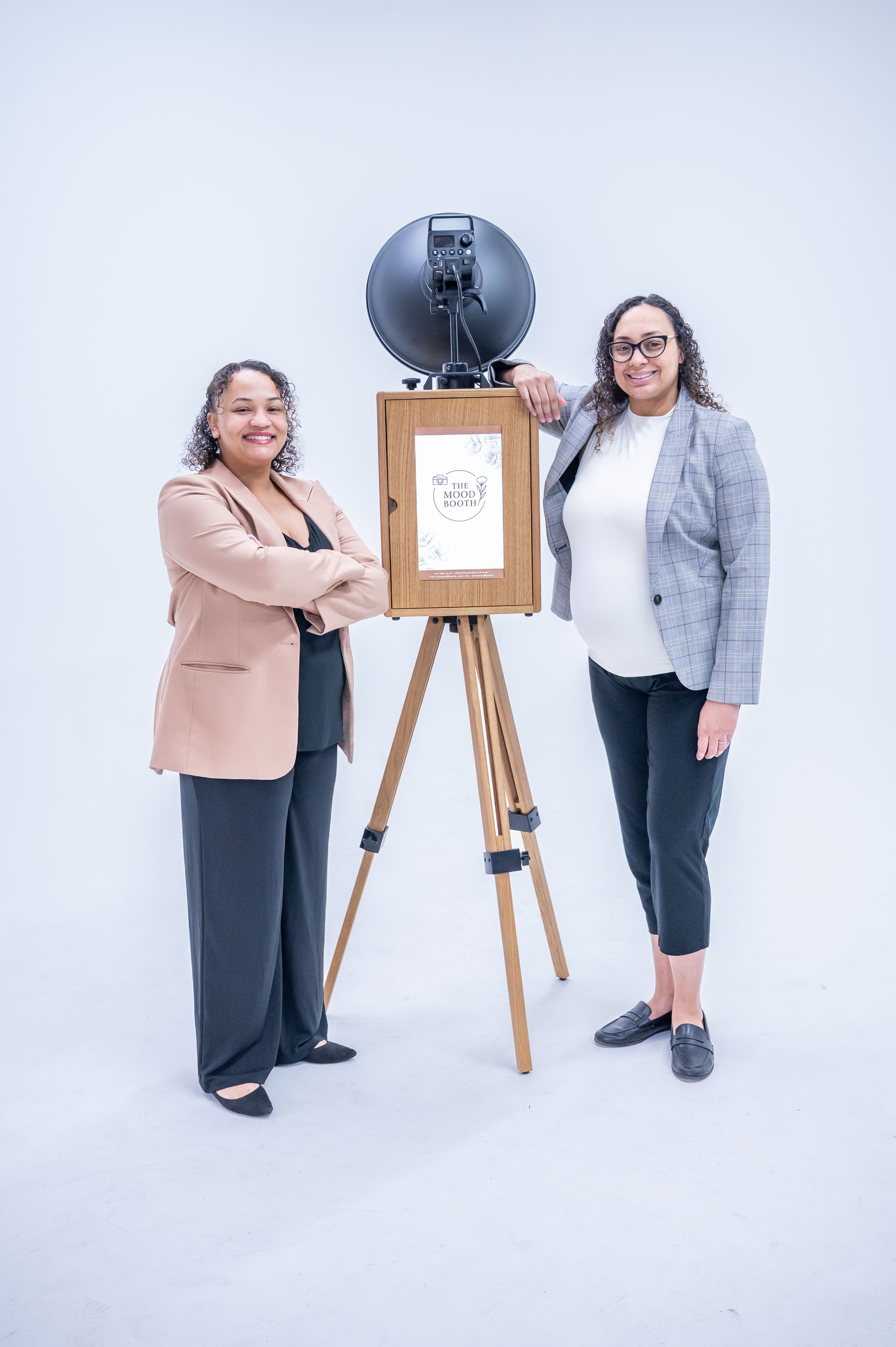 Two people stand next to a wooden easel with a display board in a studio setting against a white background.