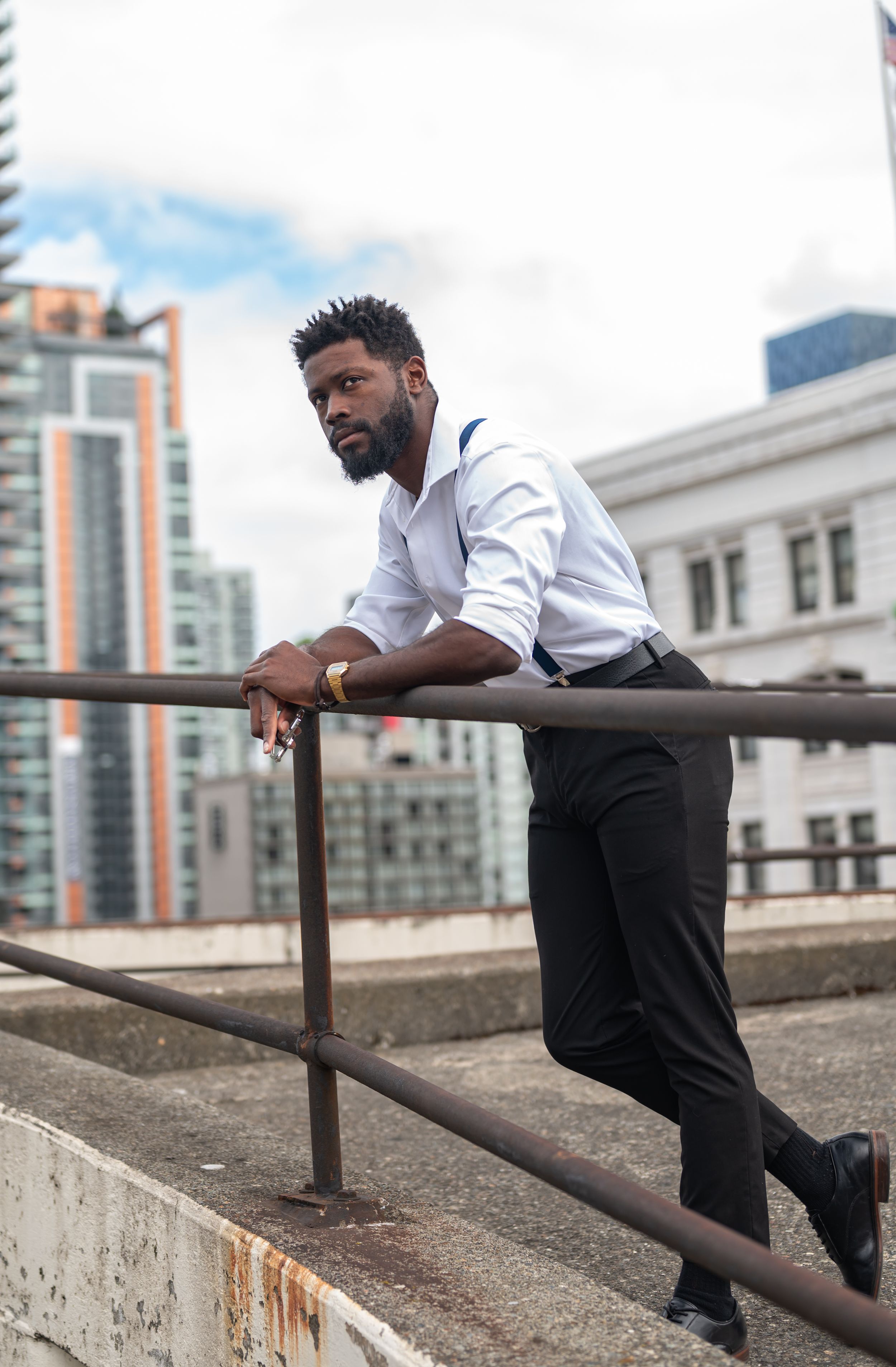 Professional dressed in white shirt and suspenders poses on urban rooftop setting.