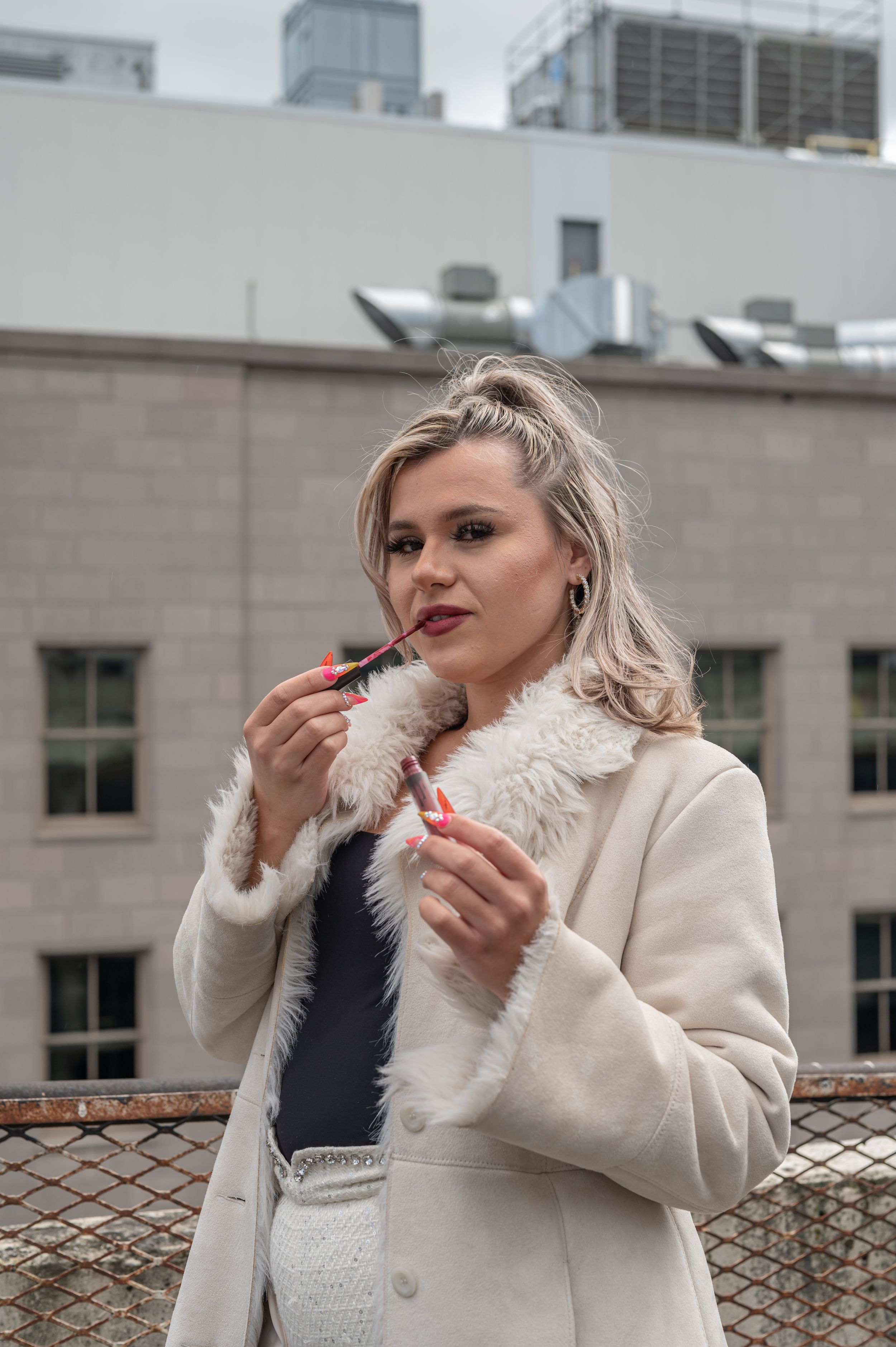 Stylish winter fashion look with cream coat and black top against urban rooftop setting.
