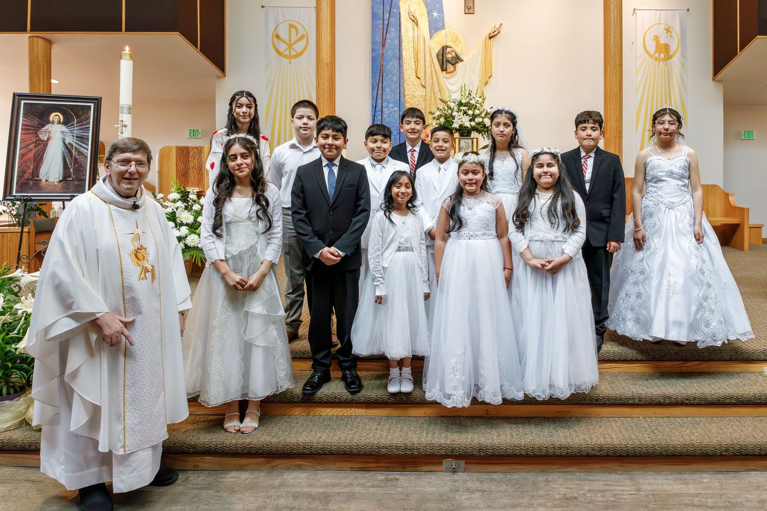 A group stands together in formal white attire with clergy at a church ceremony.