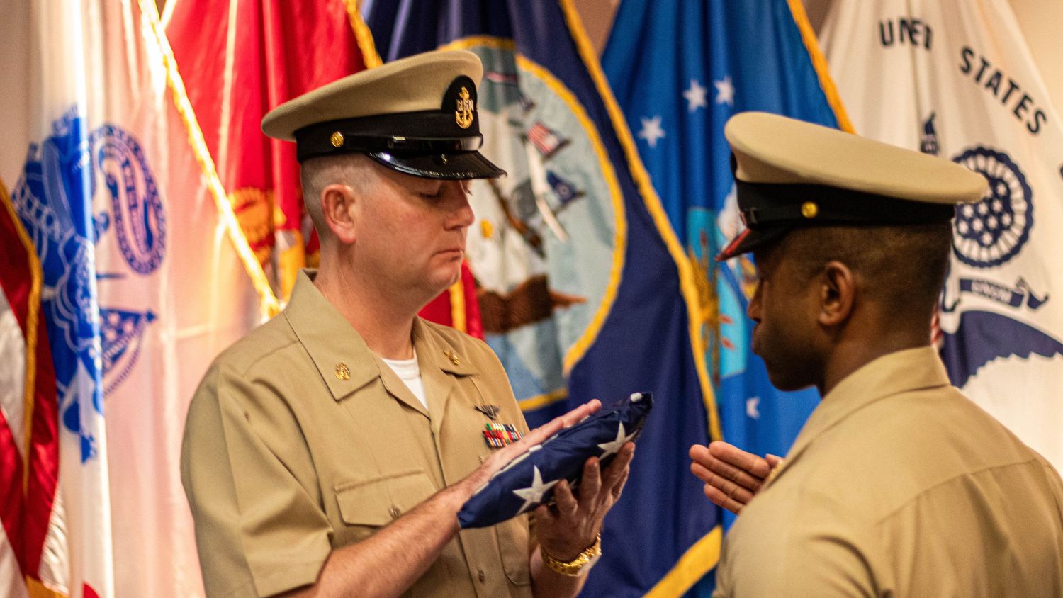 Professional military ceremony photography of a U.S. Navy Chief Petty Officer holding a folded American flag during a formal flag passing.