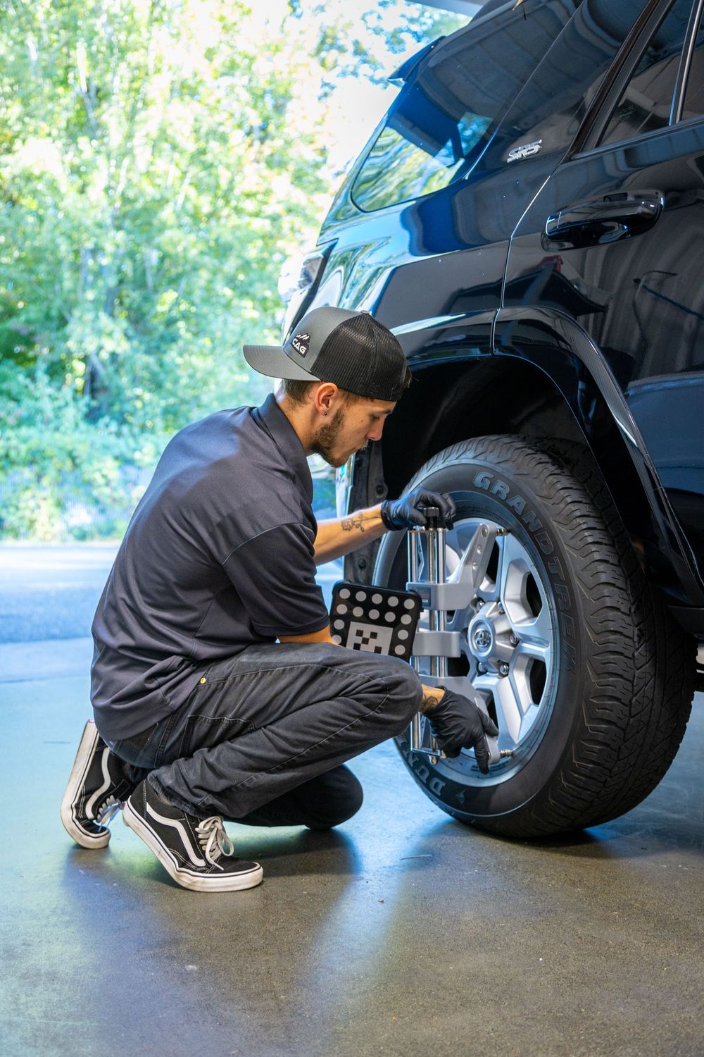 Auto mechanic performs wheel alignment service on a blue SUV using professional equipment in a repair shop.