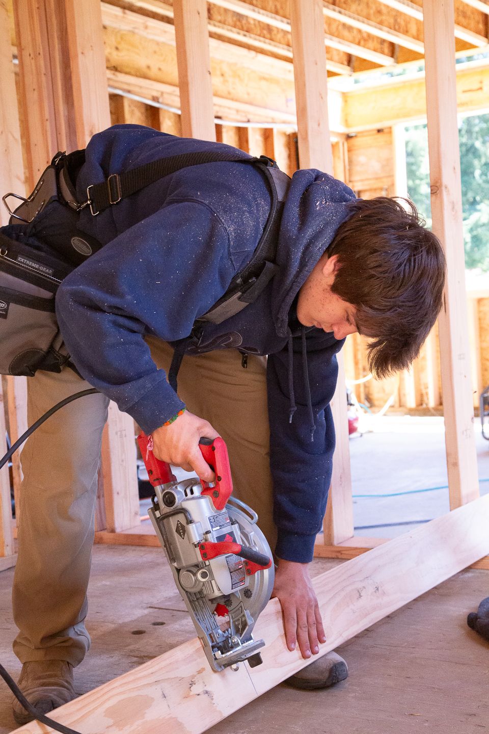Construction work on wooden beam using circular saw at residential construction site interior with exposed framing.