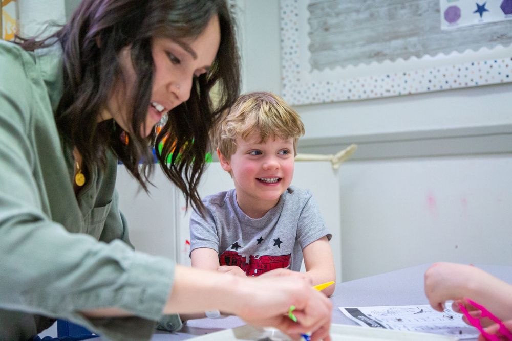 A teacher and student work together at a desk while looking at learning materials.