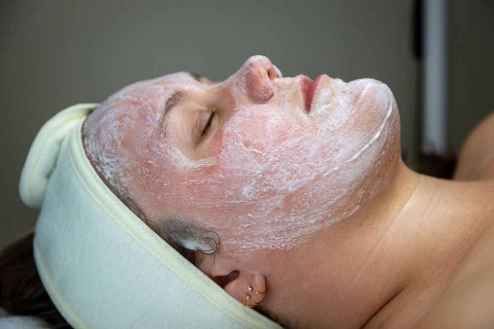Woman receiving a spa facial treatment with a pink clay mask applied to her face, lying on a massage table.