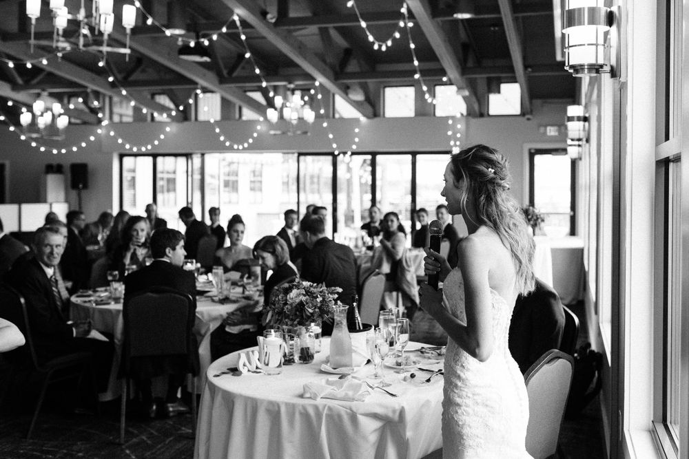 Black and white photo of a wedding reception with string lights and round dining tables.