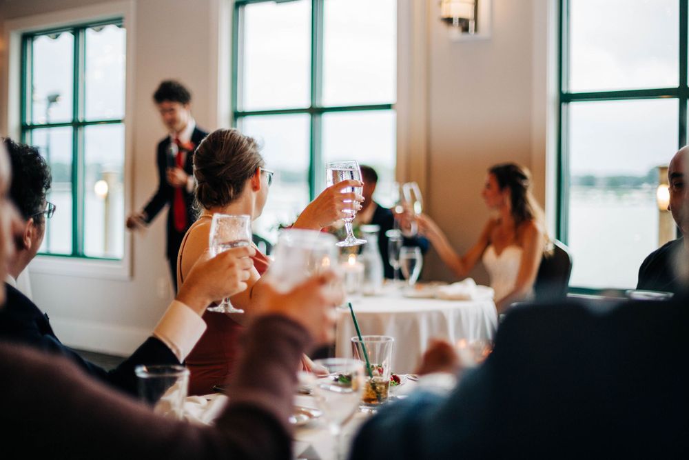 Wedding guests raise glasses in a toast during an elegant indoor reception.