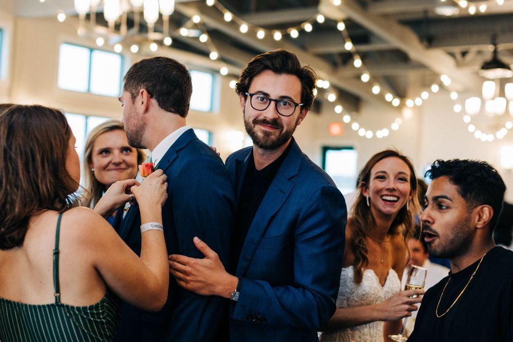 Wedding guests mingle and dance during a lively reception under string lights.